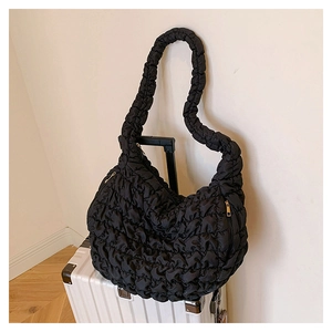 Detail of black cloud pleated tote bag with golden zipper on a white suitcase