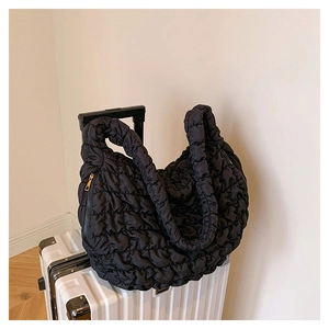 Detail of black quilted cloud tote bag with puffy texture hanging on a white suitcase