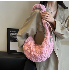 Detail of pink quilted crescent bag showing textured fabric and pleated shoulder strap