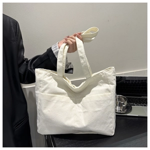 Close-up of cream corduroy tote bag with front pocket and shoulder strap detail
