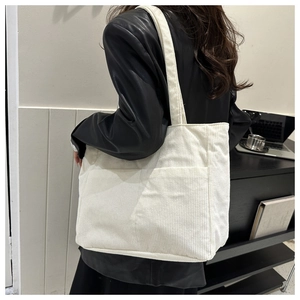 Detailed view of a white corduroy tote bag worn over the shoulder on a black coat