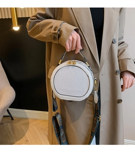 Detail of white round PU handbag featuring floral embossing and ethnic style wide strap