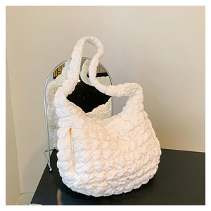 Detailed view of white quilted cloud bag with puffy texture and gold zipper on a black surface