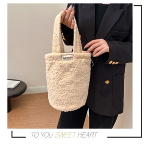 Detail view of a beige plush bucket bag with AO HUDIE branding and soft fleece texture