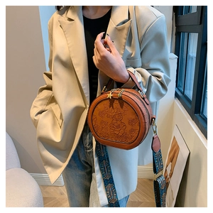 Detail of round brown leather crossbody bag with floral embossing and star charm