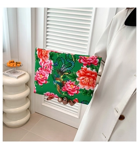 Detail of floral nylon clutch bag with phoenix pattern held by model in white coat