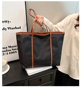 Detail of a large black nylon tote bag with brown leather handles in a home office setting