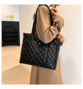 Detail of the glossy black quilted tote bag with silver magnetic closure on a shoulder strap