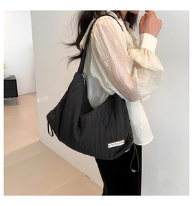 Detail of black pleated shoulder bag with Superior label on a model in indoor setting