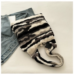 Detailed view of plush zebra print tote bag on neutral fabric with lifestyle props