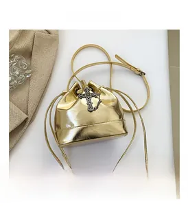 Detail of gold patent leather bucket bag with silver cross charm and drawstring