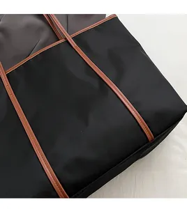 Detail of black nylon tote bag with premium brown leather straps and fine stitching work