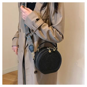 Detail of round black PU leather handbag with floral embossing and ethnic style strap