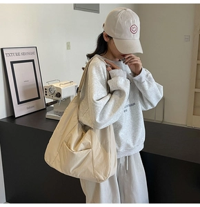 Detail view of large beige canvas crossbody bag styled with casual urban streetwear outfits