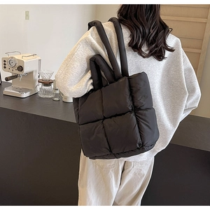 Rear view of a model wearing a large black quilted down tote bag in a cozy cafe setting