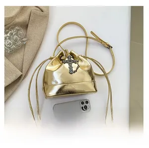 Detail of metallic gold bucket bag with vintage cross pendant and drawstring closure
