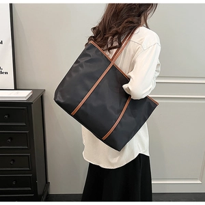 Modern black nylon tote bag with brown leather trim shown on a model in a minimalist room