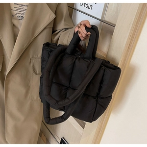 Detail shot of a black quilted down fabric handbag with padded top handles and puffy texture