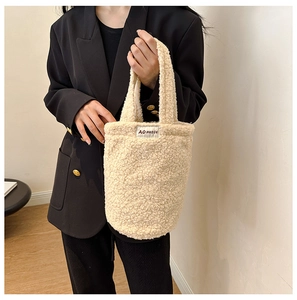 Detail of cream plush faux shearling handbag with AO HUDIE label held by a model