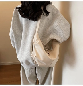 Borsa hobo beige minimalista con pieghe e tracolla larga mostrata indossata da una modella
