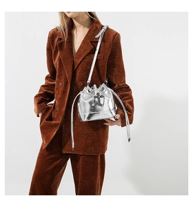 Detail of silver metallic bucket bag with black cross ornament and glossy finish
