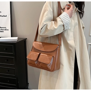 Close-up of brown vintage PU leather handbag with two small front pockets on a beige coat