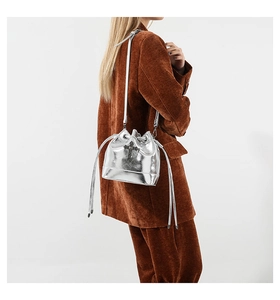 Silver metallic bucket bag with black gothic cross shown on a model in brown suit