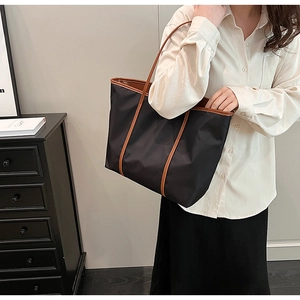 Detail of minimalist black nylon tote bag with brown leather trim and slim shoulder strap