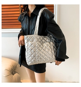 Silver quilted tote bag with metallic finish shown on shoulder with black leather outfit