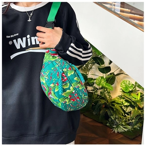 Detail of tropical floral print crossbody bag featuring green nylon fabric and woven strap