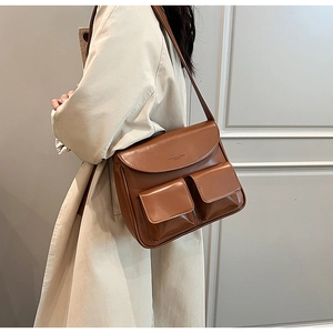 Detail of vintage brown PU leather shoulder bag with dual front pockets on stylish trench coat