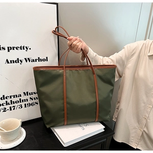 Detail view of army green nylon tote bag with brown leather handles in a lifestyle setting