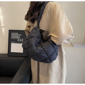 Detail of black quilted puffer hobo bag with knotted strap worn over a beige trench coat