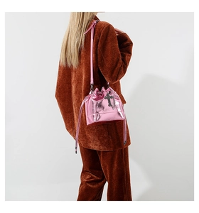 Detail of pink metallic bucket bag with cross charm and drawstring on a shoulder strap