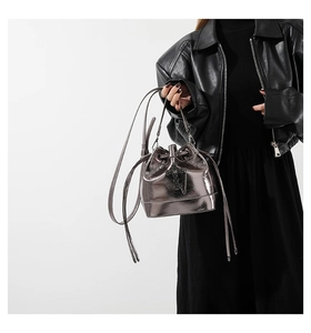 Detail of silver metallic bucket bag with drawstring and black cross chain charm