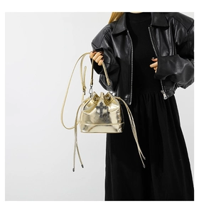 Macro detail of metallic gold bucket bag with black gothic cross accent and drawstring closure
