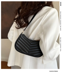 Detail of chevron quilted faux leather handbag worn over a white suit jacket