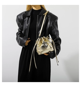 Detail of gold metallic drawstring bucket bag with black cross emblem on leather jacket