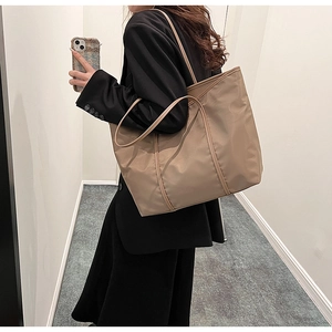 Khaki nylon tote bag with reinforced stitching worn by a model in a minimalist setting