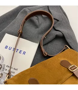 Detail view of brown suede messenger bag with adjustable leather strap on a grey blazer