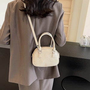 Detailed view of cream-white semicircular handbag worn over a classic gray blazer