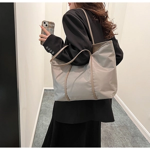 Lifestyle shot of woman carrying large nylon shoulder bag with slender straps in light grey