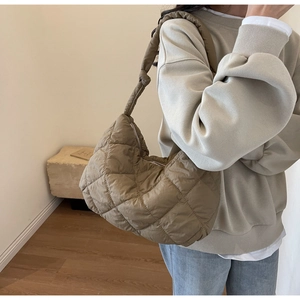 Detail of a brown quilted puffer shoulder bag with a stylish knot handle and crescent shape