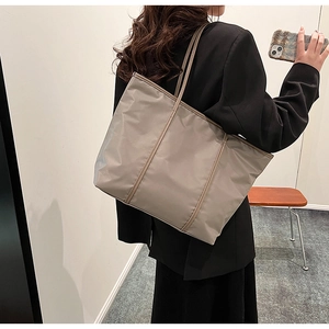 Close-up of a large khaki nylon tote bag worn on shoulder by a model in formal attire