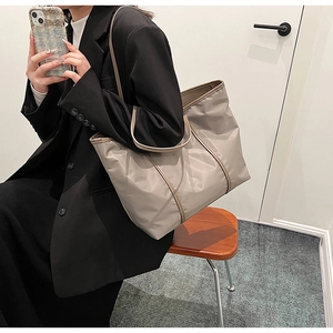 Detail view of large nylon tote bag with tan trim styled on a black blazer