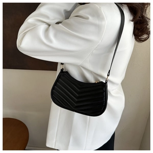 Detail of black V-quilted faux leather shoulder bag worn over a white blazer