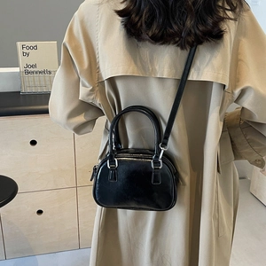 Detail showing the glossy black PU leather shoulder bag worn over a classic beige trench coat
