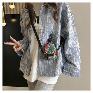 Mini green canvas floral crossbody bag with zip detail worn by a fashion model