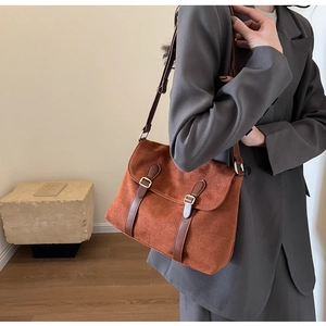 Side view of model wearing a brown suede flap messenger bag with leather straps