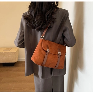 Close-up of brown suede crossbody bag with leather straps and gold buckles on a model